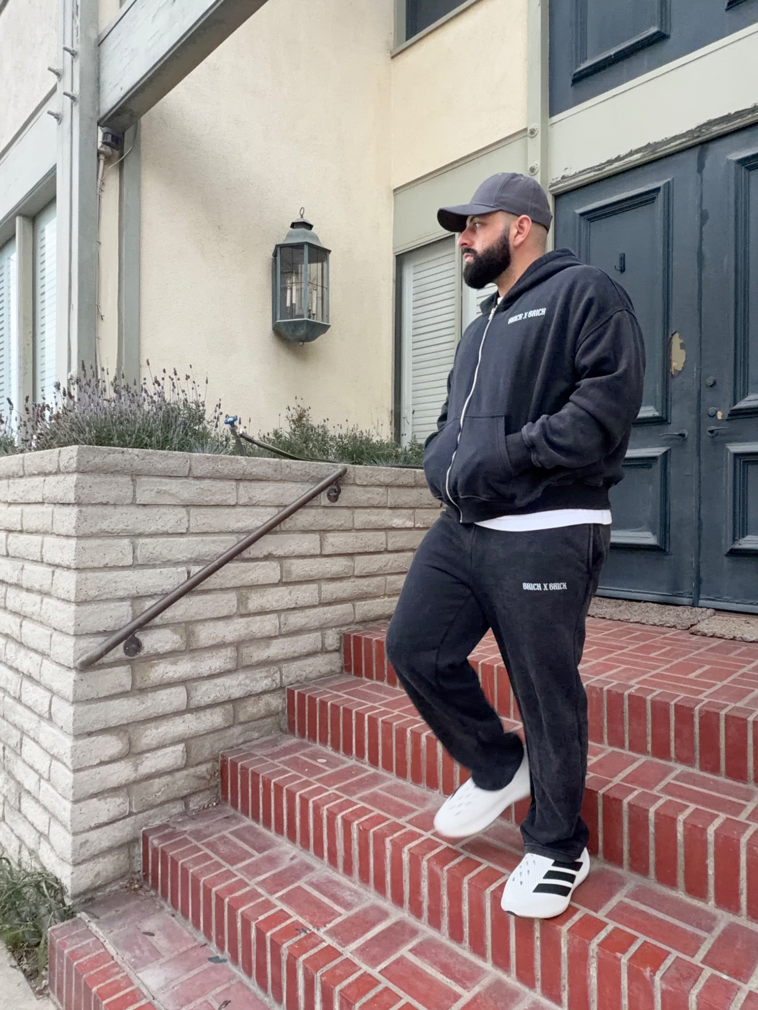 Model wearing a charcoal Brick X Brick zip hoodie and sweatpants on brick steps