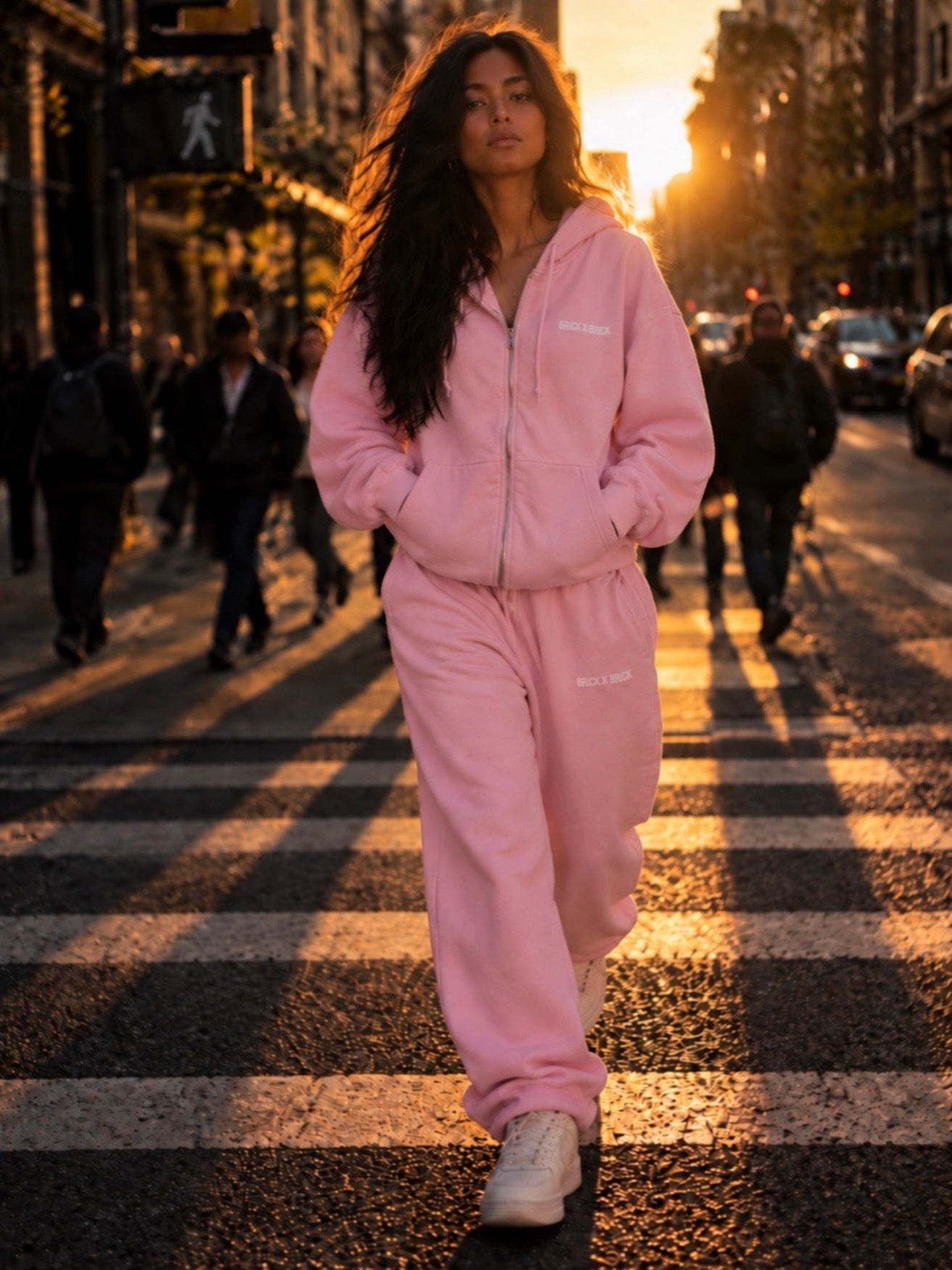 Woman wearing a pink Brick X Brick zip hoodie and sweatpants on a city street