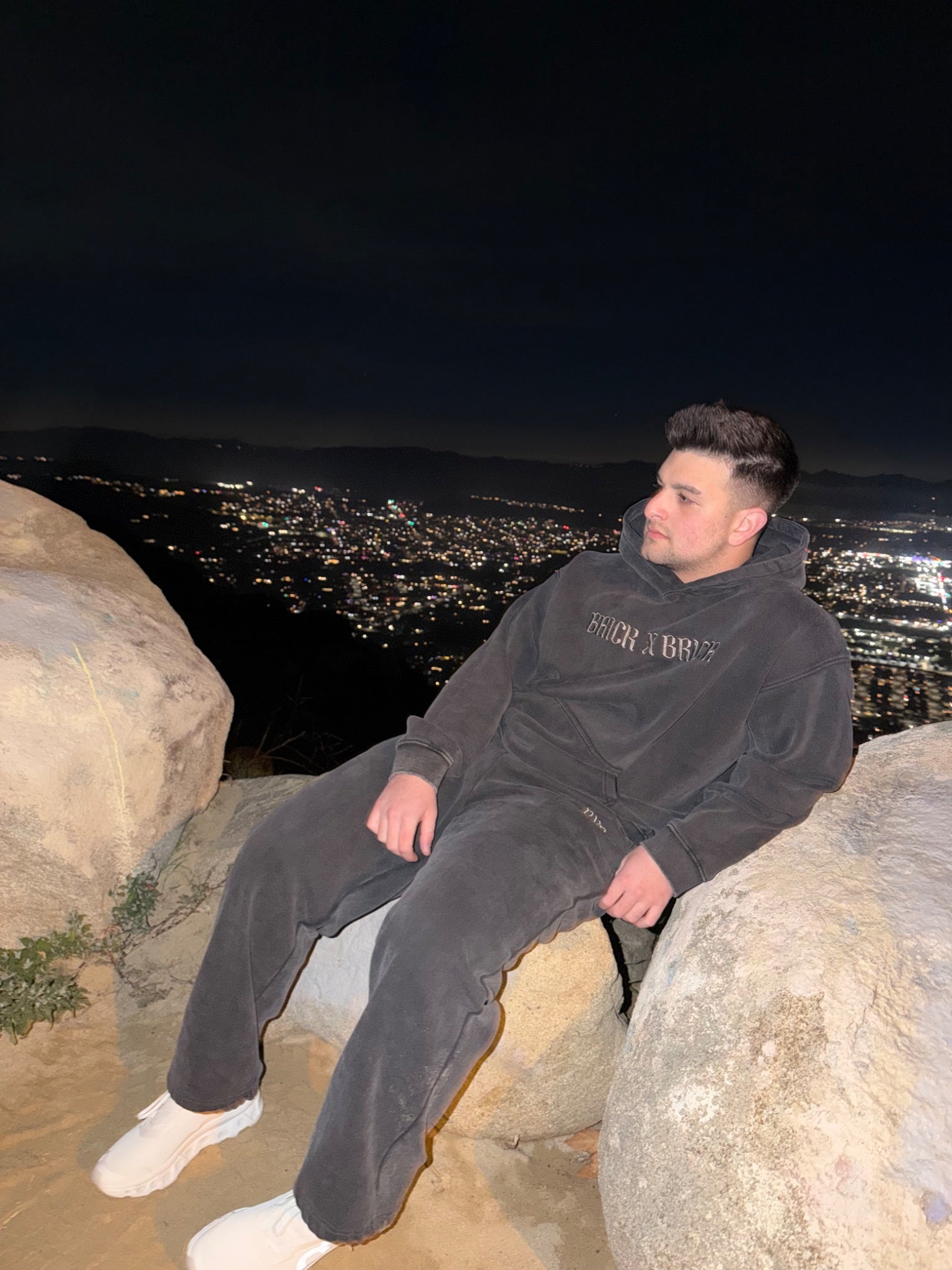 Model wearing a charcoal Brick X Brick pullover hoodie and sweatpants at night